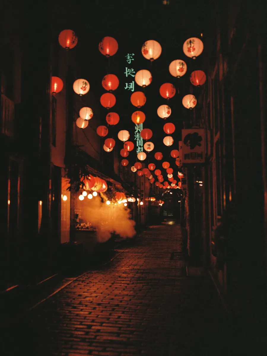 A narrow alley lined with glowing paper lanterns at night