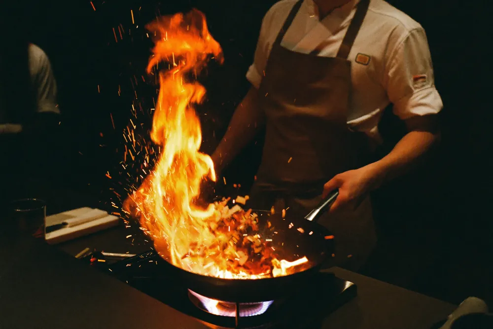 A chef tossing a wok over an open flame