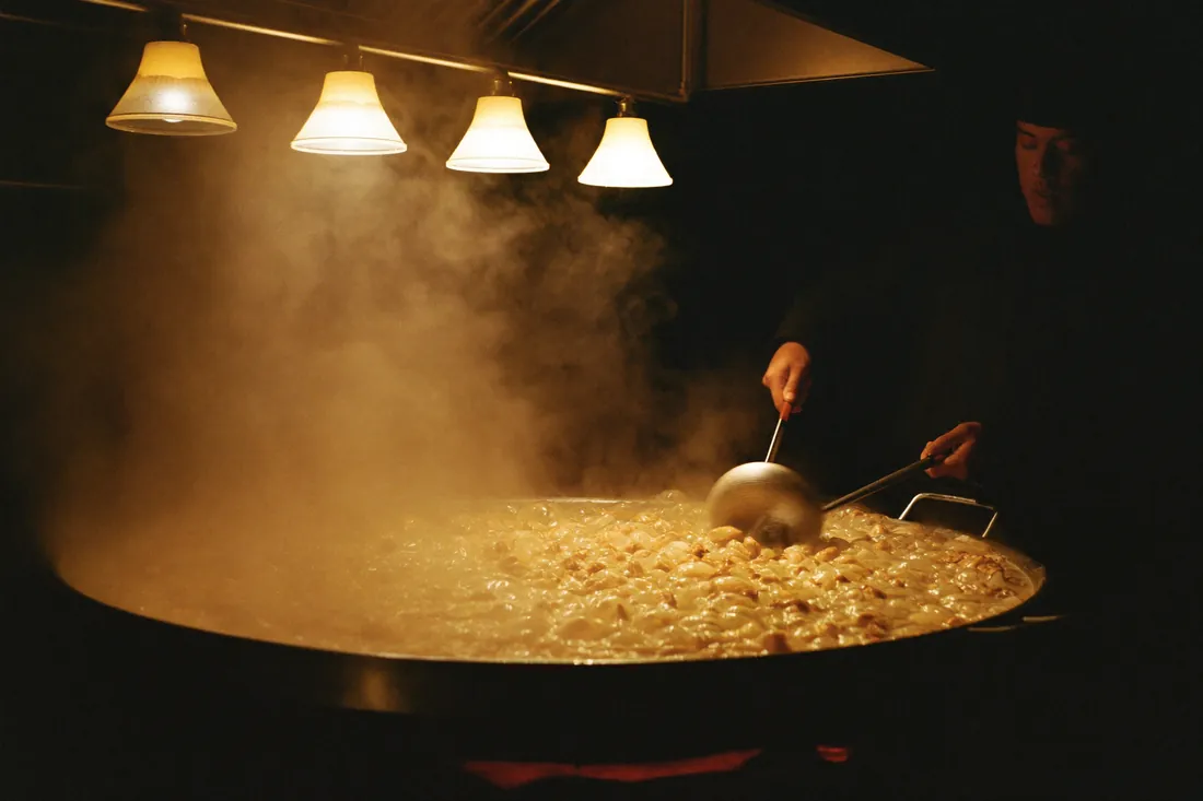 A chef stirring a large pot of simmering tonkotsu broth in a dark kitchen